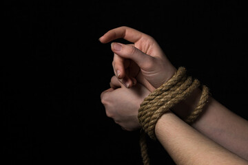 Women's hands tied with a rope on a black background.