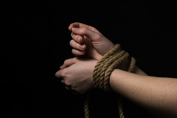 Women's hands tied with a rope on a black background.