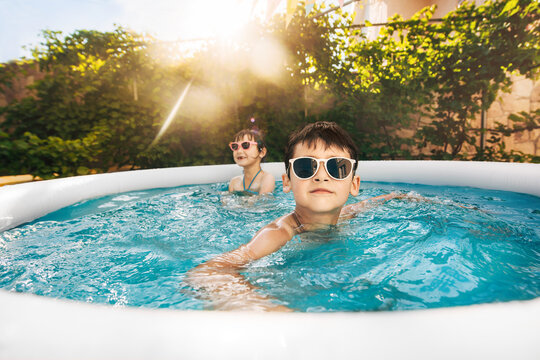 Two kids boy and girl swim in inflatable circle pool on summer sunny day outdoors on home yard. Summer vacation and healthy lifestyle concept. Close up. Wide angle shooting.