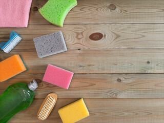 Obraz na płótnie Canvas Dishwashing liquid, brushes and kitchen sponges lie on boards. Top view. Accessories for cleaning at left on wooden light background. Concept housework. Flatlay. Mockup for advert. Copy space.