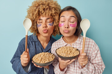 Horizontal shot of two women stand with closed eyes folded lips have cereals for breakfast awake...