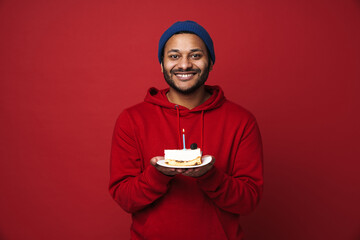 Cheerful indian man holding birthday cake with candle isolated over red background