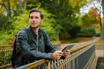 Young man using digital tablet while standing in autumn park