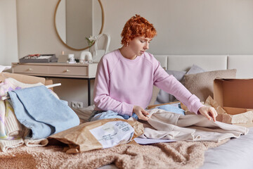Indoor shot of redhead woman prepares delivery box folds jumper sells clothes prepares online...