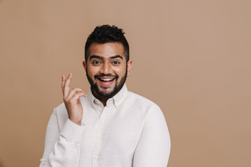 Smiling indian guy gesturing while standing isolated over beige wall