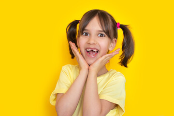 Close-up portrait of surprised or exited cute little toddler girl with missing baby tooth smile having fun on yellow background with copy space. 