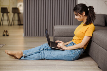 Happy indian or arabian young woman sitting on floor and working by laptop