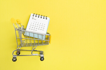 Shopping cart toy and calendar from the supermarket on table with yellow background, Sale buy mall market shop consumer concept. Copy space