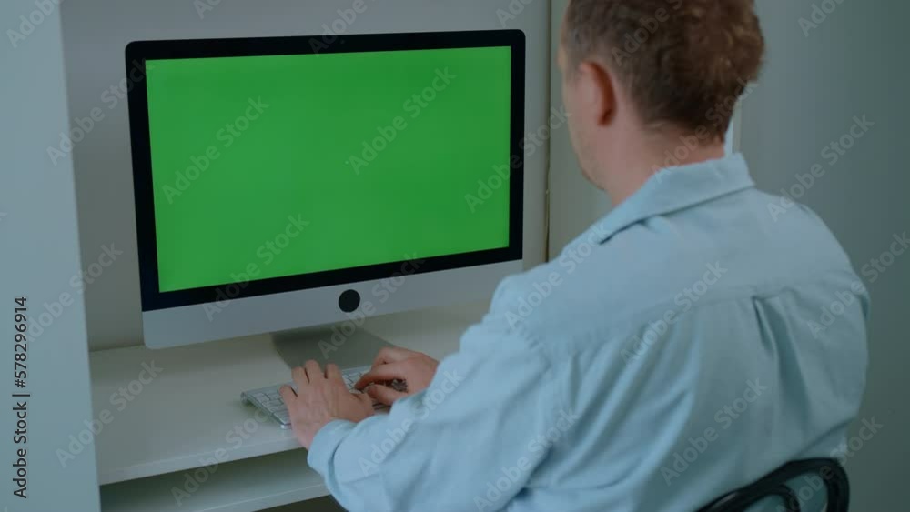 Poster rear view man sitting at the workplace typing on white keyboard display with green screen freelancer