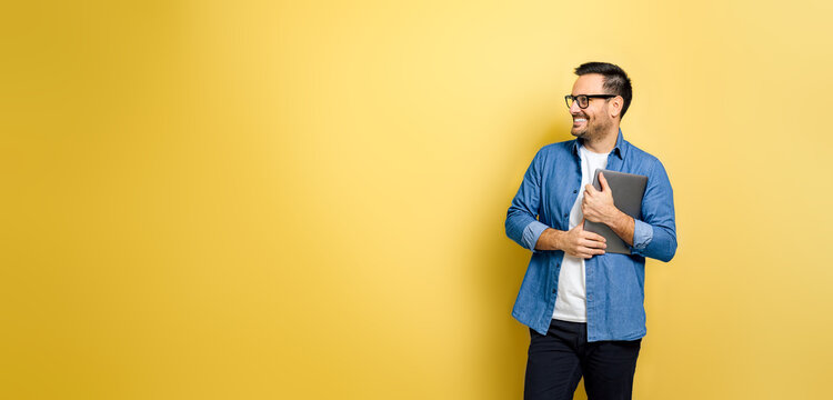 Man holding laptop looking away smiling against yellow background
