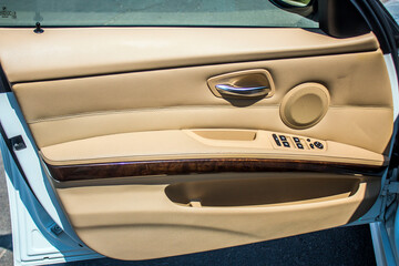 Black window regulator buttons and speaker on the beige upholstery of the front door of the car