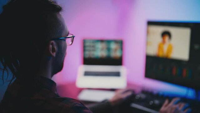 Young man in glasses working on video editing on computer doing montage and color correction. Professional man hand making edits on a special panel. Concept of creating video content.