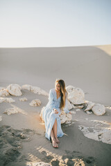 Woman with long hair in a stylish dress poses in the desert sands.