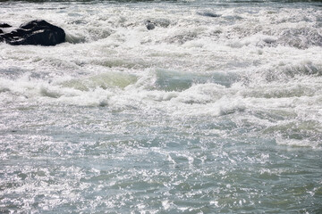 Powerful turbulent stream of cold mountain river in summer. Fast current along the rapids of muddy...