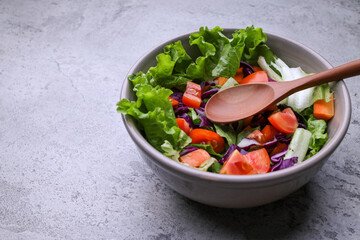 Healthy vegan lunch bowl made from various raw fresh vegetables on gray background. Lettuce tomato and red cabbage. Top view