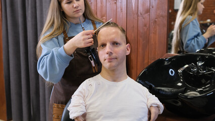 Fototapeta na wymiar a hairdresser girl in a beauty salon does a haircut and hair styling for a man with disabilities.