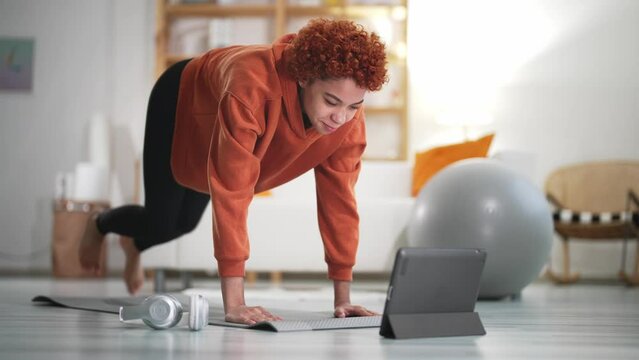 Cheerful active girl doing fitness at home, using tablet, watching online lessons on Internet. Sport wellness lifestyle concept. Weight loss, muscle building. Health lifestyle.
