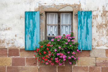 Fototapeta na wymiar Altes Fenster mit blauen Fensterläden und Blumenschmuck