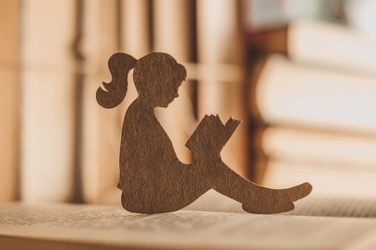 A female child reads a book in the home library. Silhouette of a girl with cardboard reading children's fairy tales