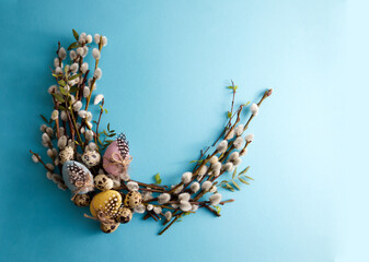 Bouquet of spring willow decorated with Easter eggs and quail eggs on a blue background copy space