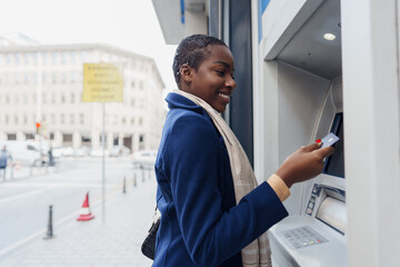 Young african woman withdrawing cash at the ATM - obrazy, fototapety, plakaty