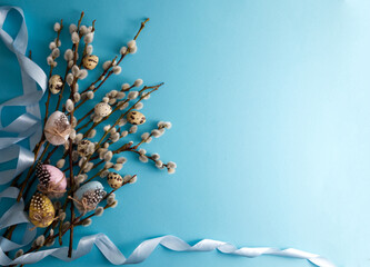 Bouquet of spring willow decorated with Easter eggs and quail eggs on a blue background copy space