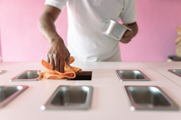 An ice-cream parlor worker is cleaning the shop counter with a cleaning cloth before opening