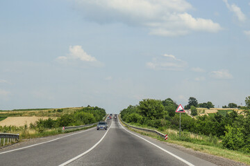 Straight two-lane road against the backdrop of picturesque landscape. Greenery by the road. Summer, travel, cars. Photo, country landscape, Ukraine