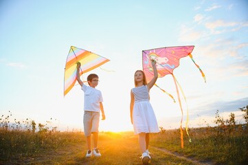 Happy boy and girl playing with kites in field at sunset. Happy childhood concept.