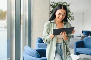 Young modern female freelancer in airport lounge or business center and works using digital tablet, creating new design project