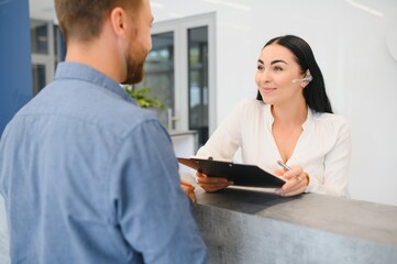 The employee of the beauty salon meets the client in the reception of a modern beauty salon. A man signs a paper with the consent for maintenance. The woman smiles at him
