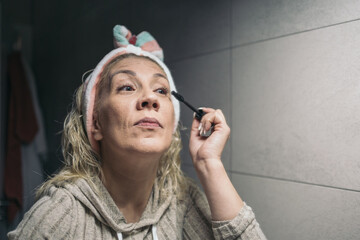 Middle-aged blonde woman applying eye makeup in her bathroom.