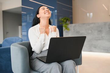 Portrait of excited young caucasian woman celebrating success while sitting with laptop at home or...