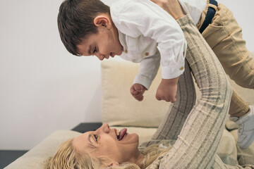 Cropped image of a middle-aged blonde woman lying on the sofa holding her young son who has special...