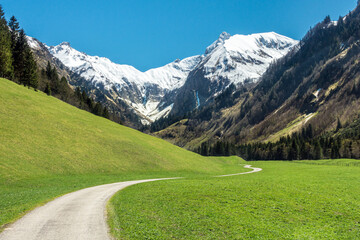 Beautiful landscape with snow capped mountains, green grass meadows and hiking trail in springtime. Trettachtal, Allgaeu, Bavaria, Germany. - 578312516