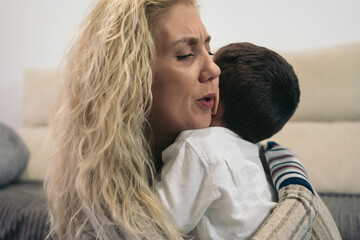 Middle-aged blonde woman emotionally embracing her young autistic son because he is crying.