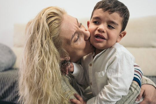 Middle-aged blonde woman emotionally embracing and kissing her young autistic son because he is crying.