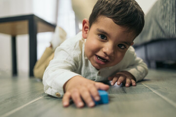 Frontal image of a young autistic child on the living room floor playing with a piece of blue wood.