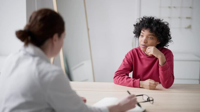 Young woman, patient clinic, to cabinet at consultation tells therapist complaints and disease. Female doctor listens and writes, makes notes for delivery diagnosis. Concept medical help, health care.