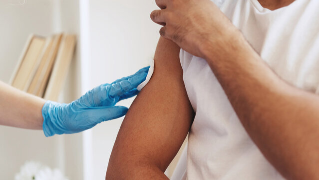 Flu shot. Vaccine inoculation. Virus prevention. Closeup of unrecognizable doctor hand in glove giving injection jab dose to male patient arm shoulder.