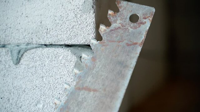An old manual hacksaw for aerated concrete close-up against the background of a wall of aerated concrete bricks. Saw and gas block