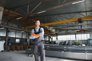 Portrait of factory worker in protective uniform and hardhat standing by industrial machine at...