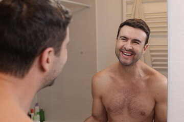 Fototapeta na wymiar Cute shirtless man looking at his reflection in the bathroom 