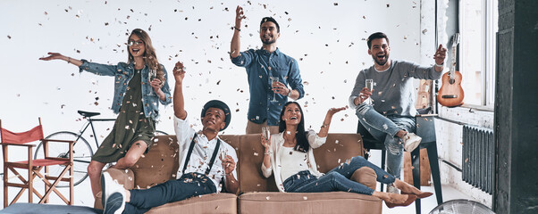 Group of young people throwing confetti and smiling while relaxing at home together