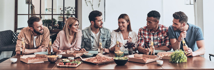 Group of cheerful young people having dinner with pizza indoors together