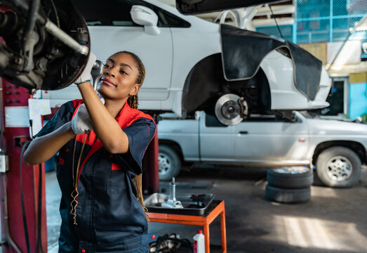 Engineer team checking under car condition on lifter in garage.Young auto mechanic in uniform is looking at camera and smiling examining car...