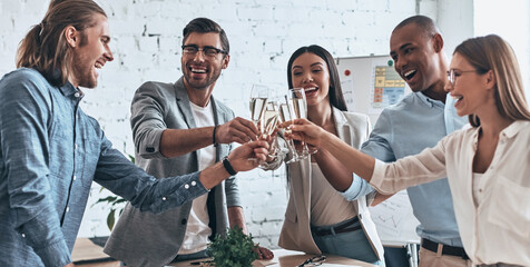 Group of cheerful business people toasting with champagne while standing in office together
