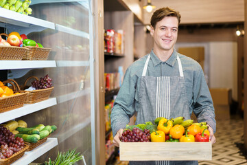 Happy cheerful caucasian grocery store staff arranging a vegetables and fruits on the shelf. 