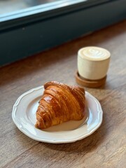 A cup of latte coffee with Croissant. Coffee break on wooden table by the window. Morning healthy breakfast.