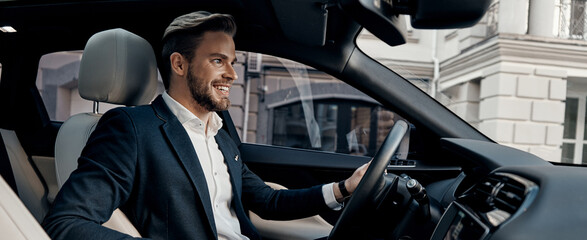 Handsome young man in formal wear smiling while driving a car